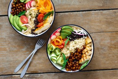 İki Buda kase. Temiz ve dengeli sağlıklı gıda kavramı. Tavuk ızgara biftek, pirinç, baharatlı nohut, siyah ve beyaz quinoa, avokado, havuç, kabak, turp, domates ahşap masa üstü görünümü