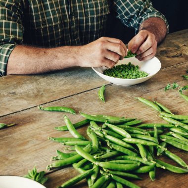 Temiz yeşil bezelye mutfakta ahşap masada oturan erkek eller. Rustik tarzı. Ahşap masa üzerinde kase yeşil bezelye