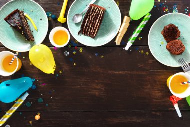 Çerçeve çikolatalı kek ve dekorasyon partisi düz kahverengi ahşap zemin üzerinde yatıyordu. Üstten görünüm Çocuk Doğum günü tablo kavramı