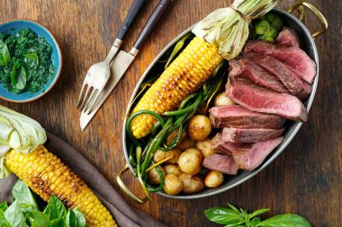 Dilim Dana biftek tavada kızarmış Mısır, patates ve yeşil fasulye fesleğen sos, üstten görünüm ahşap tablo ile servis