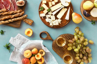 Şarap aperatifler: üzüm, şeftali, kayısı, armut, elma, jamon, sert peynir, brie peyniri ve Rokfor peyniri cam beyaz şarap üstten görünüm mavi taş zemin üzerine düz lay