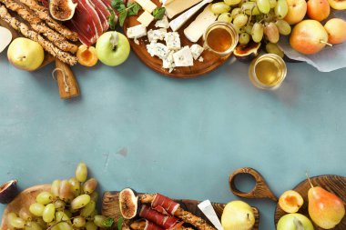 Çeşitli şarap atıştırmalıklar çerçevesinde: üzüm, şeftali, kayısı, armut, elma, jamon, sert peynir, brie peyniri ve Rokfor peyniri cam beyaz şarap üstten görünüm mavi taş zemin üzerine düz lay