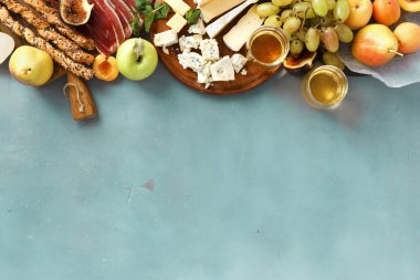 Ayarlamak beyaz cam şarap şarap aperatifler: üzüm, şeftali, kayısı, armut, elma, jamon, sert peynir, brie peyniri ve Rokfor peyniri kopya alanı üst mavi taş zemin üzerine görüntülemek düz lay