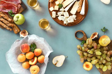 Çeşitli aperatifler şarap: üzüm, şeftali, kayısı, armut, elma, jamon, sert peynir, brie peyniri ve Rokfor peyniri cam beyaz şarap üstten görünüm mavi taş zemin üzerine düz lay