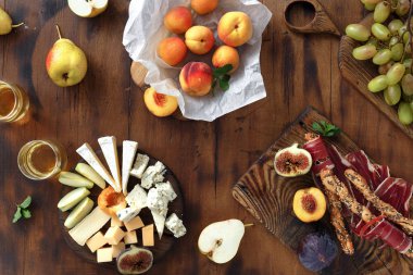 Üstten görünüm meze tablo şarap için. Çeşitli aperatifler şarap: üzüm, şeftali, kayısı, armut, elma, jamon, sert peynir, brie peyniri ve Rokfor peyniri cam beyaz şarap ile ahşap masa üzerinde düz lay