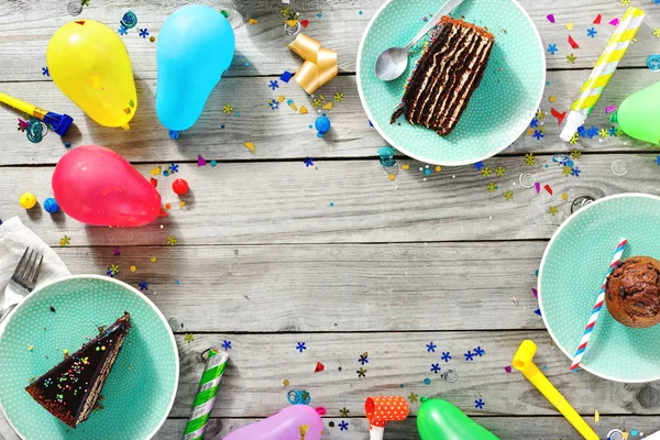 Top view children birthday table. Frame of chocolate cake, muffins and decoration party on wooden background flat lay