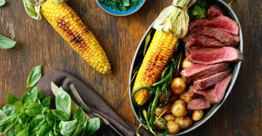 Dilim Dana biftek tavada kızarmış Mısır, patates ve yeşil fasulye fesleğen sos, üstten görünüm ahşap tablo ile servis