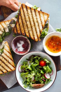 Tavuk, salata, sos ve salatalık turşusu ile ahşap kesme tahtası üzerinde roka sandviç görünümü top.