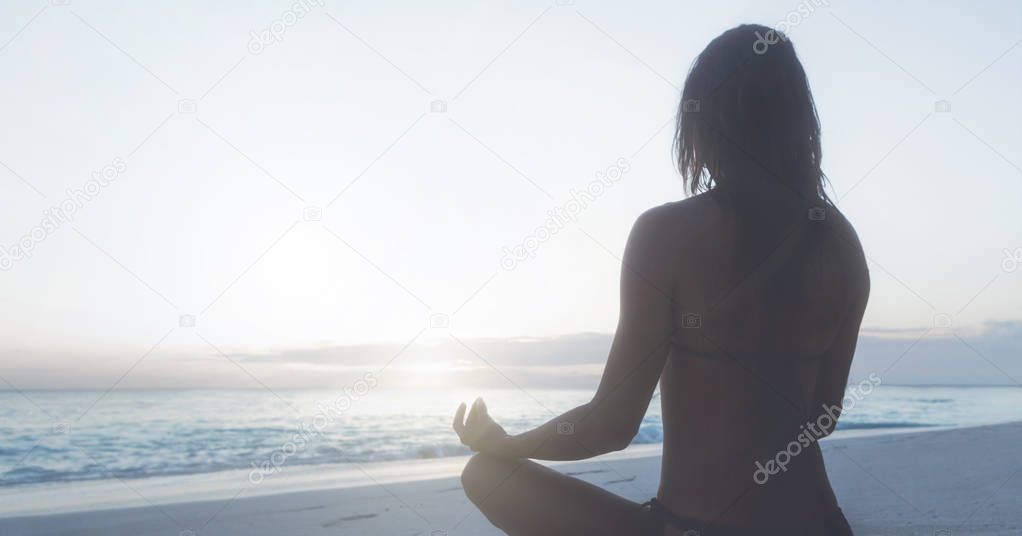 Young woman practicing yoga on beach at sunrise