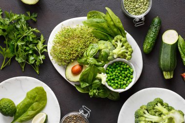 Ayarla temiz bir vejetaryen için protein kaynağı yemek yemek için sağlıklı gıda: salatalık, lucerne, kabak, ıspanak, fesleğen, yeşil bezelye, avokado, brokoli, kireç ve yeşil mercimek koyu arka planda, üstten görünüm