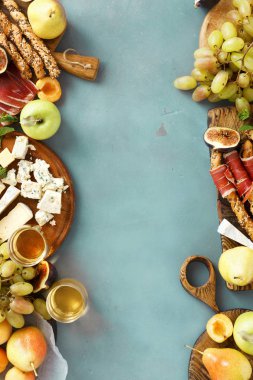 Çeşitli şarap atıştırmalıklar çerçevesinde: üzüm, şeftali, kayısı, armut, elma, jamon, sert peynir, brie peyniri ve Rokfor peyniri cam beyaz şarap üstten görünüm mavi taş zemin üzerine düz lay