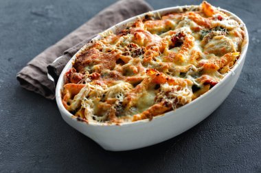 Koyu arka plan üzerinde kabak soslu tavuk, jambon ve mozzarella ve parmesan peynirli fırında makarna. İyi hissetmek için yenen yemek