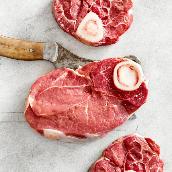 Set raw beef meat on bone with butcher knife on gray concrete background, top view, flat lay