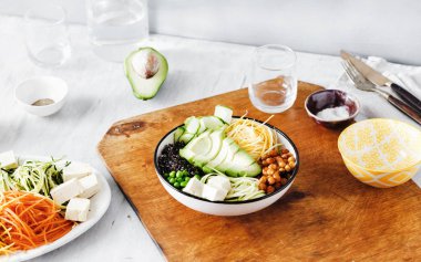 Malzemeler ahşap masa Buda kase yemek pişirmek için ayarlayın. Quinoa, nohut, soya peyniri, peynir, kabak, avokado, salatalık, spiralized sebze