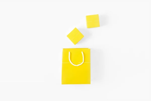 白い背景の上に小さな黄色のギフト ボックスと黄色い紙バッグ フラット レイアウトを表示します — ストック写真