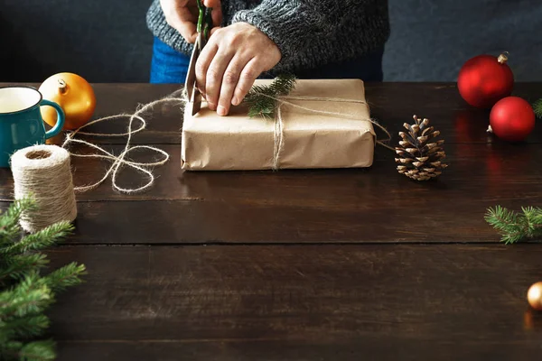 男性の手は 木製のテーブルにギフト ボックスを包装します 素朴なクリスマスの背景 折り返し表示の背景 — ストック写真