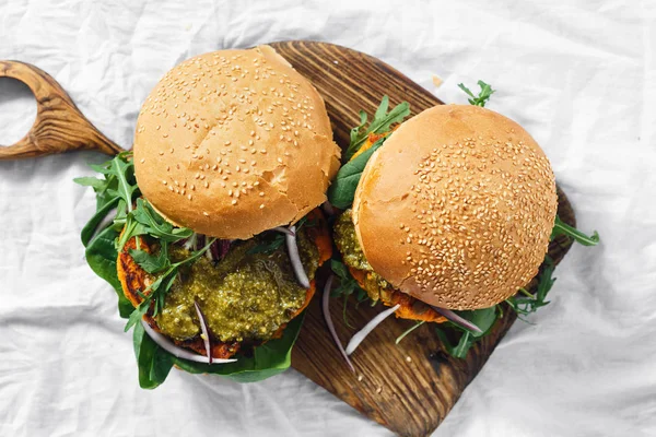 Vegetarian burger made of pumpkin cutlet, spinach, arugula and pesto sauce served on a wooden board top view. Healthy vegetarian food concept