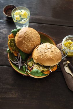 Ahşap masa tabağa vejetaryen burger kabak pirzola, ıspanak, roka ve vejetaryen pesto sos ile servis
