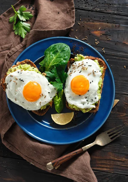 Healthy avocado toasts with fried egg in faces shape on dark wooden table