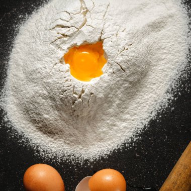 Yumurta ve yumurta sarısı siyah arka plan üstten görünüm üzerinde un yığını