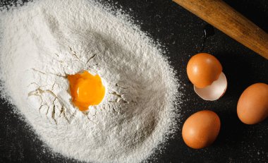 Yumurta ve yumurta sarısı siyah arka plan üstten görünüm üzerinde un yığını