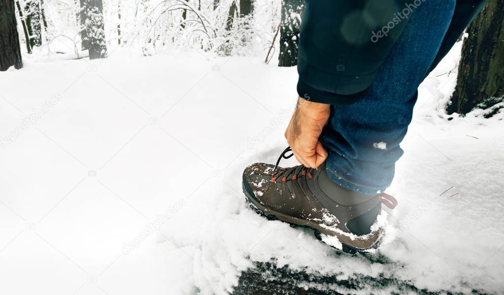Man tying shoelaces on boots in the winter in the snowy forest. Lifestyle concept