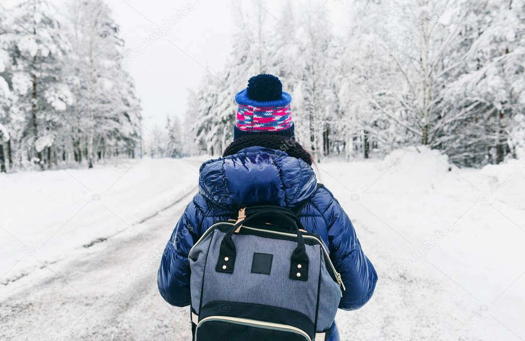 rear view of young woman with backpack in winter on snowy road in Sweden