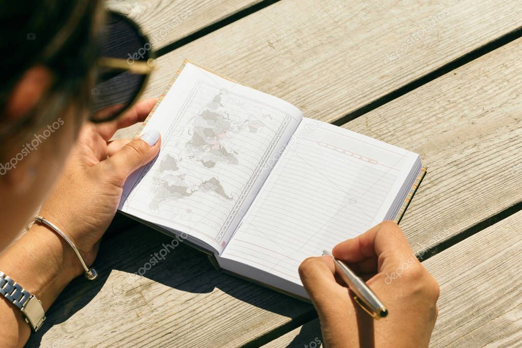 List of travel concepts. Young woman writing in notebook list of places to see
