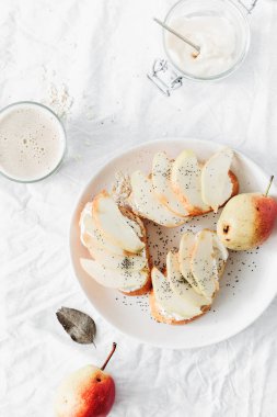 Krem peynirli sandviç, armut ve yulaf süt beyaz arka planda, üstten görünüm. Sağlıklı kahvaltı veya Aperatif