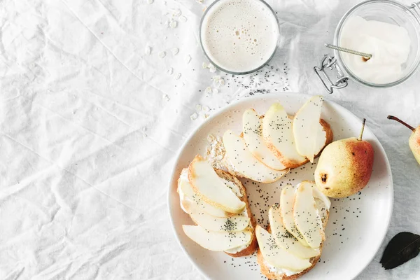Krem peynirli sandviç, armut ve yulaf sütü kopya alanı, üstten görünüm beyaz zemin üzerine. Sağlıklı kahvaltı veya Aperatif