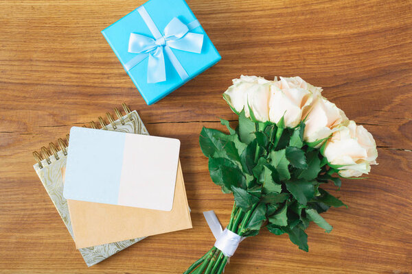 International Womens Day concept. Flower card. Bouquet of roses, gift and blank card on wooden background. Mothers Day. top view