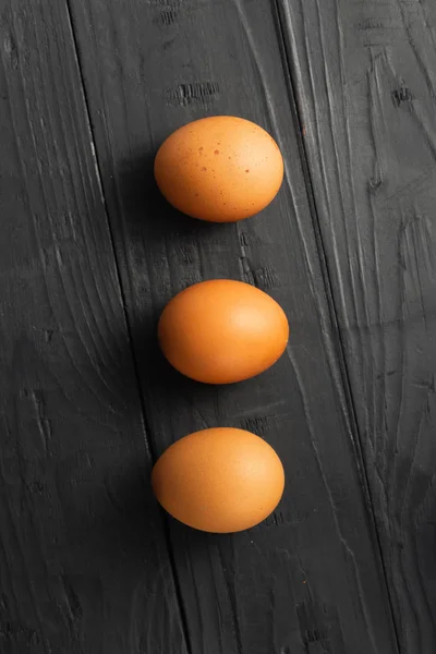 Três ovos de galinha escuro fundo de madeira vista superior — Fotografia de Stock