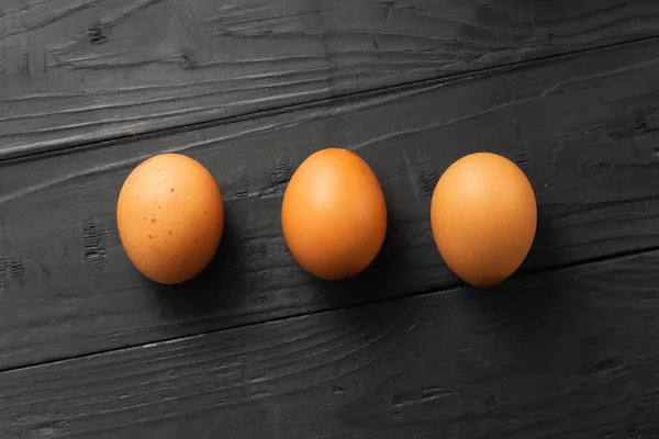 Três ovos de galinha escuro fundo de madeira vista superior — Fotografia de Stock