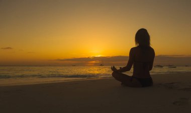 Kadınlar gün batımında okyanus sahilinde meditasyon yaparlar.