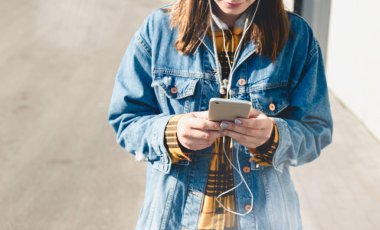 Sosyal medyayı akıllı telefonlarında kullanan genç ve mutlu bir kadın şehirde yürüyor.