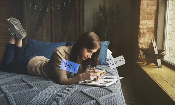 Happy young woman in bed at home on couch texting her friend