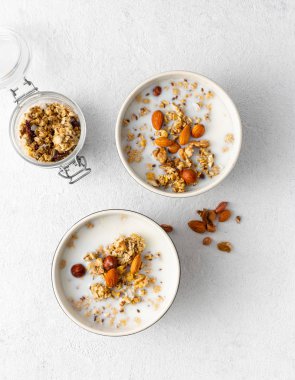 Beyaz bir arka plan üzerinde kase meyve, fındık, süt ve fıstık ezmesi ile Granola kahvaltı. Sağlıklı kahvaltılık gevrek üst görünümü 
