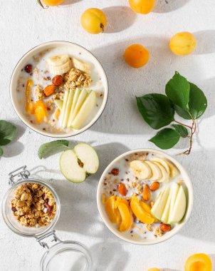 Beyaz bir arka plan üzerinde kase meyve, fındık, süt ve fıstık ezmesi ile Granola kahvaltı. Sağlıklı kahvaltılık gevrek üst görünümü 