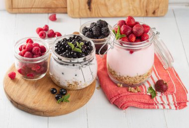 Ev mutfağında ahşap tahta üzerinde cam kavanoz ev yapımı çilek, yaban mersini, böğürtlen ve ahududu ile sağlıklı kahvaltı tahıl