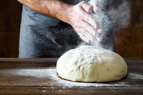 Man preparing bread dough on wooden table in bakery