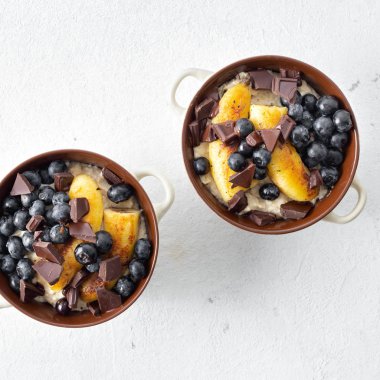 Beyaz arka plan üst görünümünde kızarmış muz, çikolata ve yaban mersini ile plaka yulaf ezmesi ile kahvaltı masası 