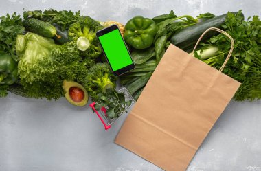 Bakkal alışveriş konsepti. Kağıt torba, alışveriş sepeti ve yeşil sebzeler ile metin mesajı veya tasarım için boş ekranlı akıllı telefon Sağlıklı gıda satın alın