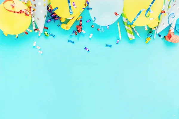 Birthday balloon background with colorful party streamers, confetti and birthday party hats blue bacground top view