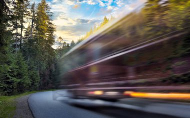 Bulanık otobüs gün batımında sonbahar ormanında dağ yolunda ilerliyor. Seyahat kavramı