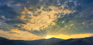 Gün batımının güzel olduğu dağlar. Parlak batan güneş bulutları delip geçiyor.
