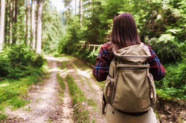 Arkaya bakan genç bayan turist ormanda sırt çantasıyla yürüyor. Seyahat ve yaz tatilleri açık hava yaşam tarzı konsepti 