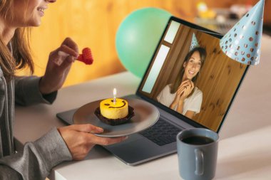 Smiling young woman celebrating her birthday at home with to your sister or girlfriend online on video call isolation because pandemic COVID-19. Funny female giving birthday cupcake with candle  clipart