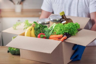 Teslimatçı, ev mutfağında karton kutular ve yiyecek tutuyor. Güvenli teslimat konseri
