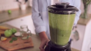 Genç bir kadın evdeki mutfakta yeşil detoks smoothie 'den sağlıklı bir kahvaltı hazırlıyor.