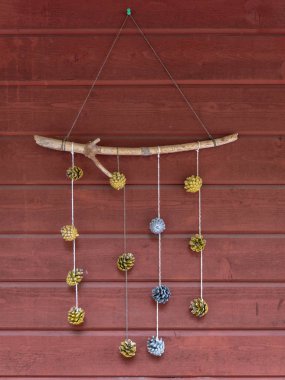 Handmade decoration of colourfully painted pine cones hanging on a stick against the red wall clipart